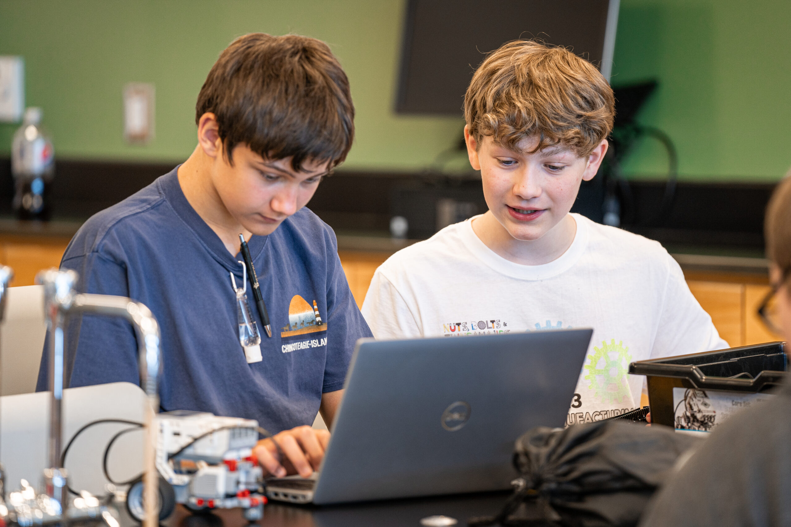 Two students look at a laptop computer with a robot next to them.