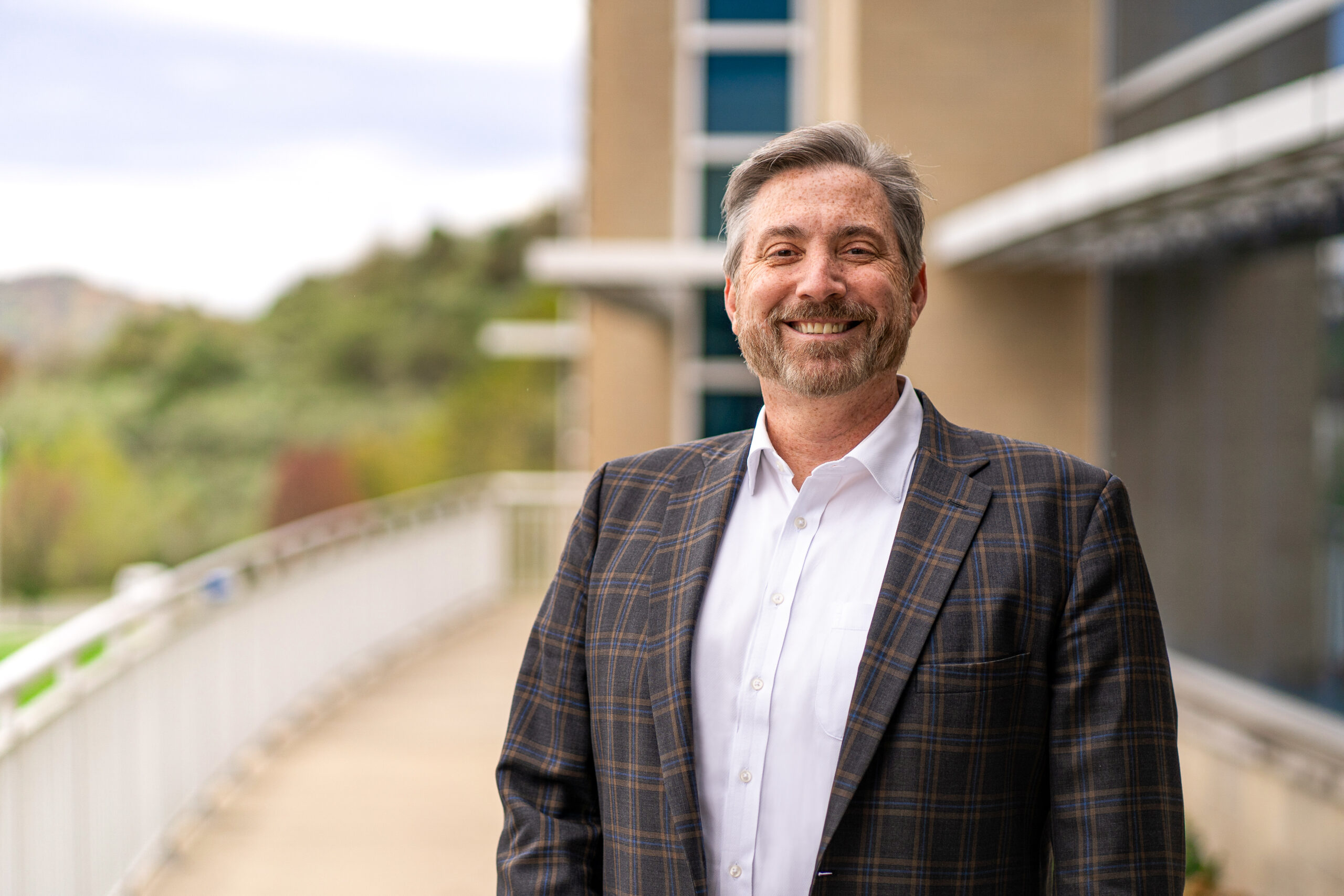 Pierpont President Milan Hayward is pictured wearing a plaid suit jacket with a white shirt standing in front of Pierpont's Advanced Technology Center.