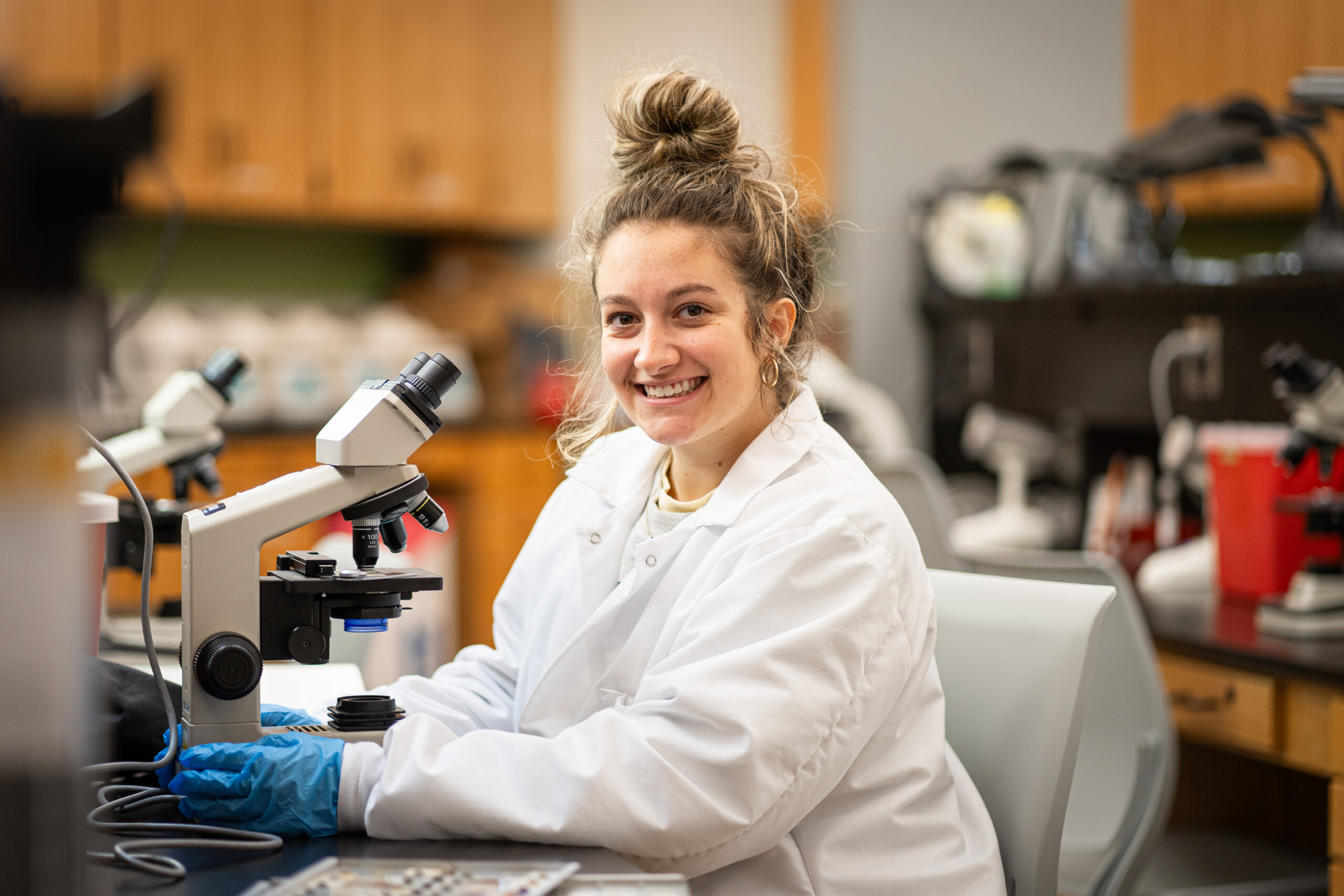 Pierpont Community and Technical College Medical Laboratory Technology student, Grace Rome, smiles for a photo wearing a white lab coat in a lab setting.