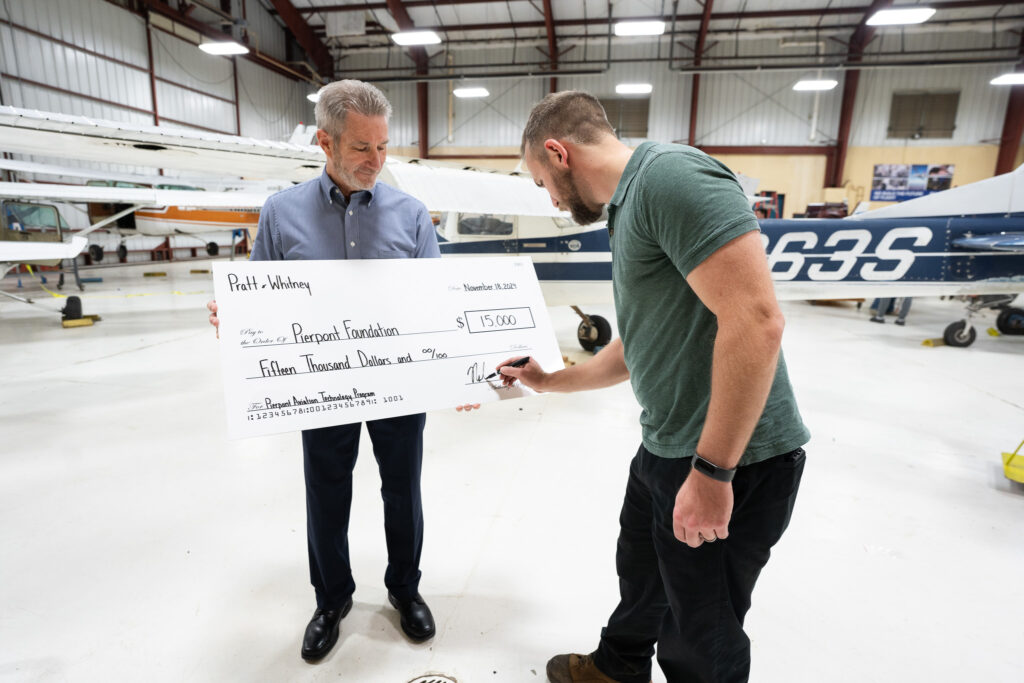 A representative from Pratt and Whitney signs the donation check held by Director of Aviation Technology, Brad Gilbert.