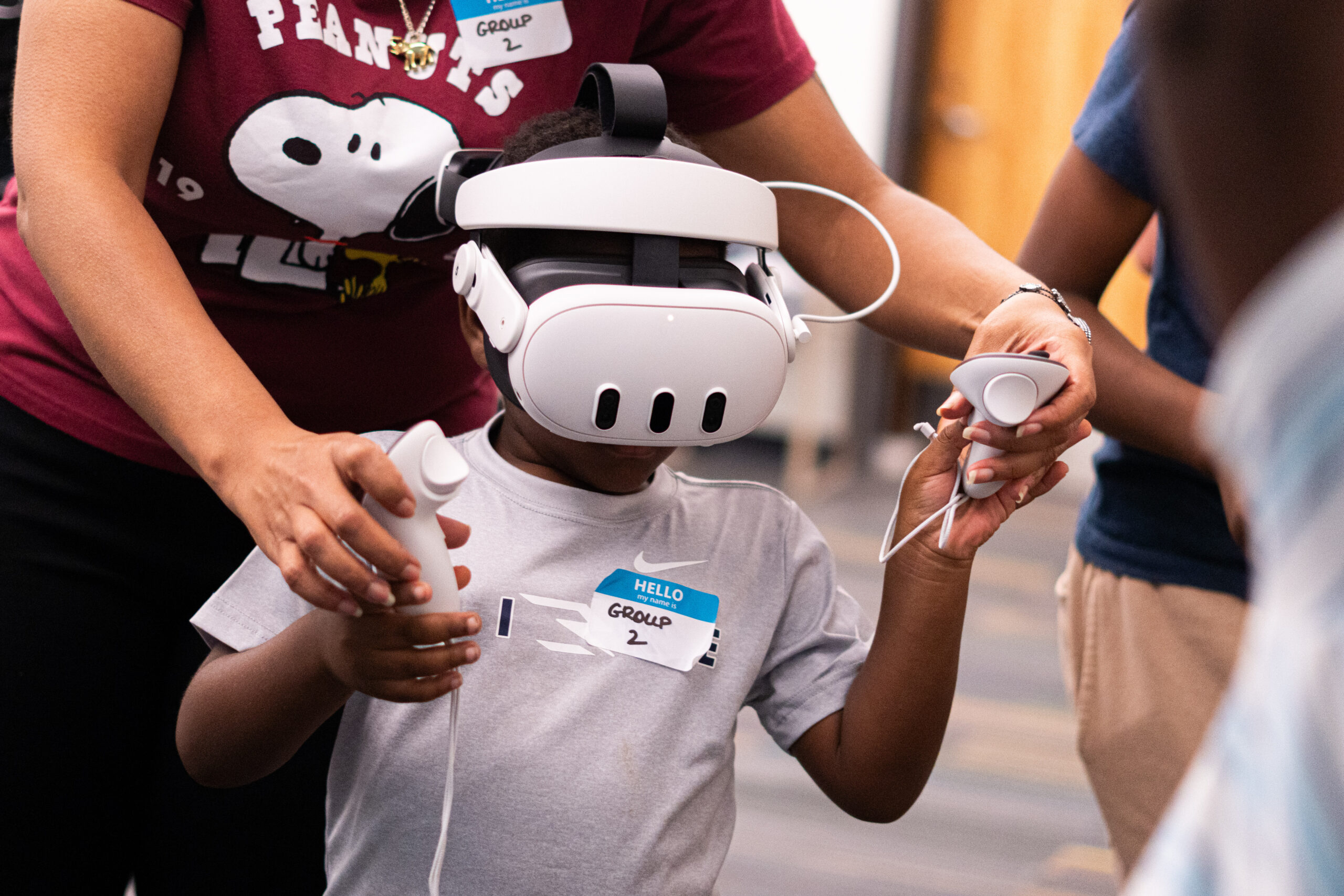 A person wearing a virtual reality headset and holding controllers, with hands guiding them from behind.